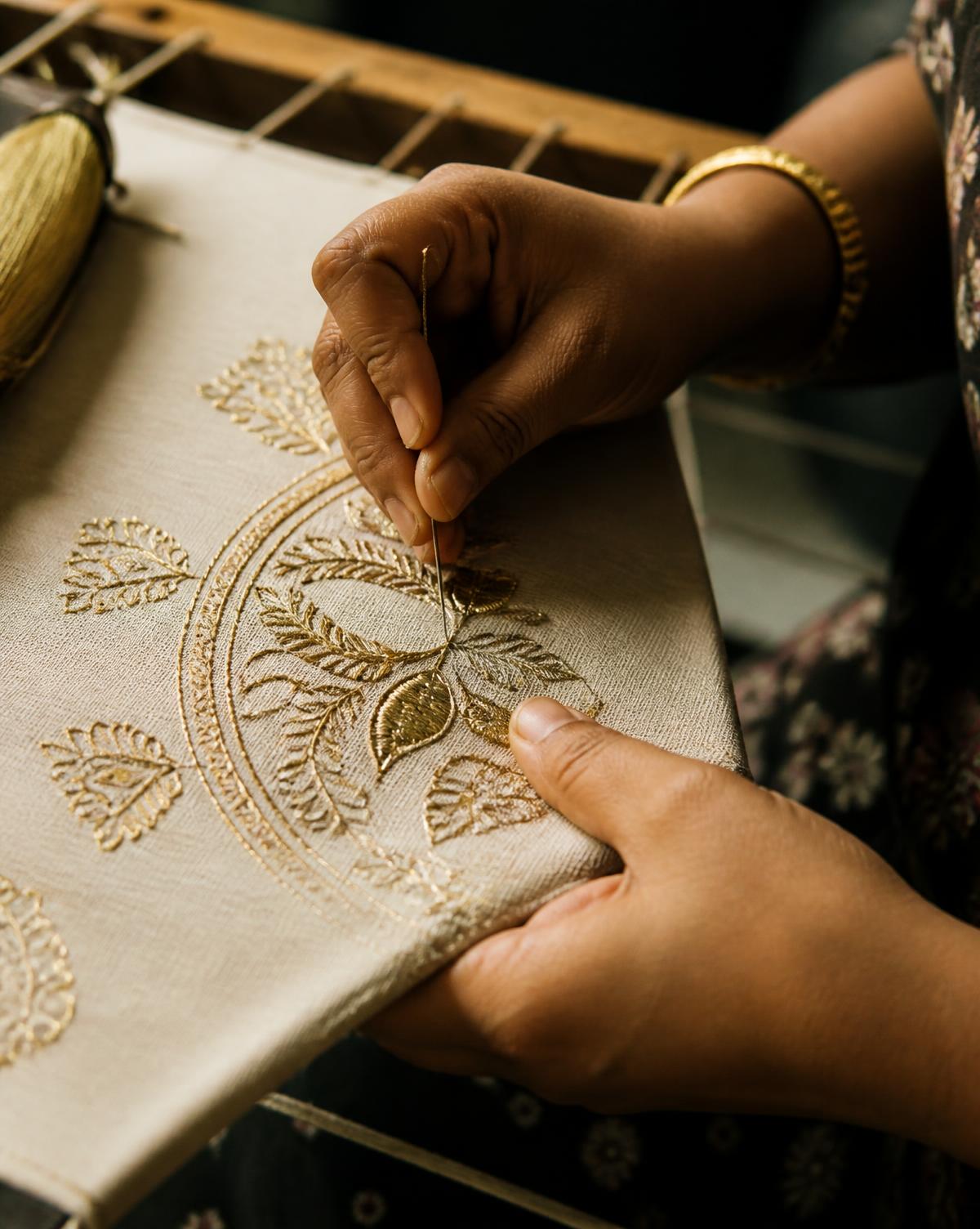 An artisan working gold zari hand embroidery on a stretched fabric frame